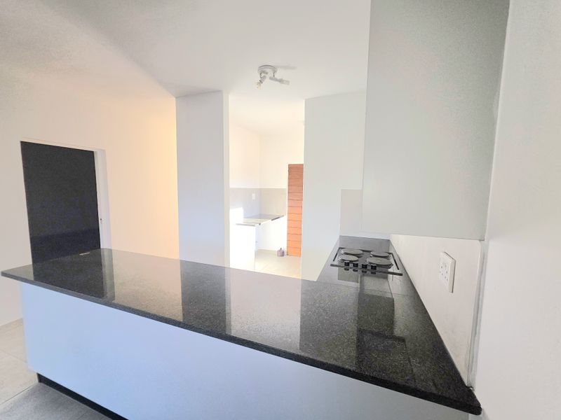 A clean, modern kitchen featuring dark granite countertops, a built-in hob, and neutral cabinetry, offering a functional and bright workspace.
