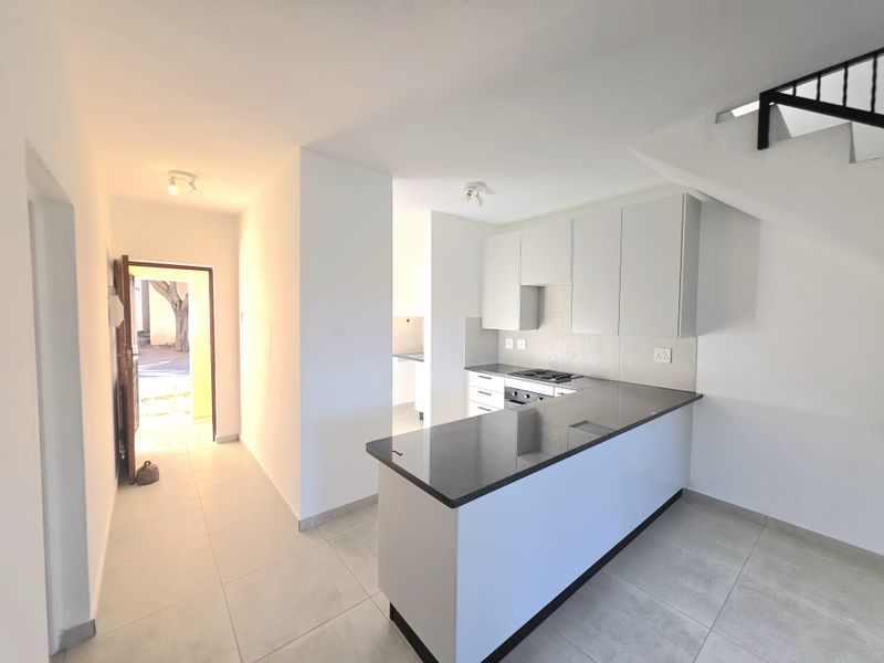 Modern kitchen featuring granite countertops, built-in cabinetry, and integrated appliances, seamlessly connected to the entrance area and staircase.