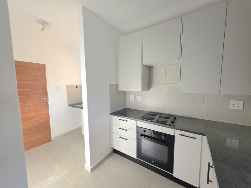 Modern kitchen featuring clean white cabinetry, dark stone countertops, built-in oven, and electric hob, with an adjacent scullery area.