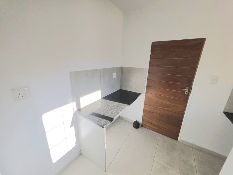 A clean, minimalist scullery or utility area featuring a granite countertop, tiled splashback, and neutral floor tiles, providing a functional prep or wash-up space.