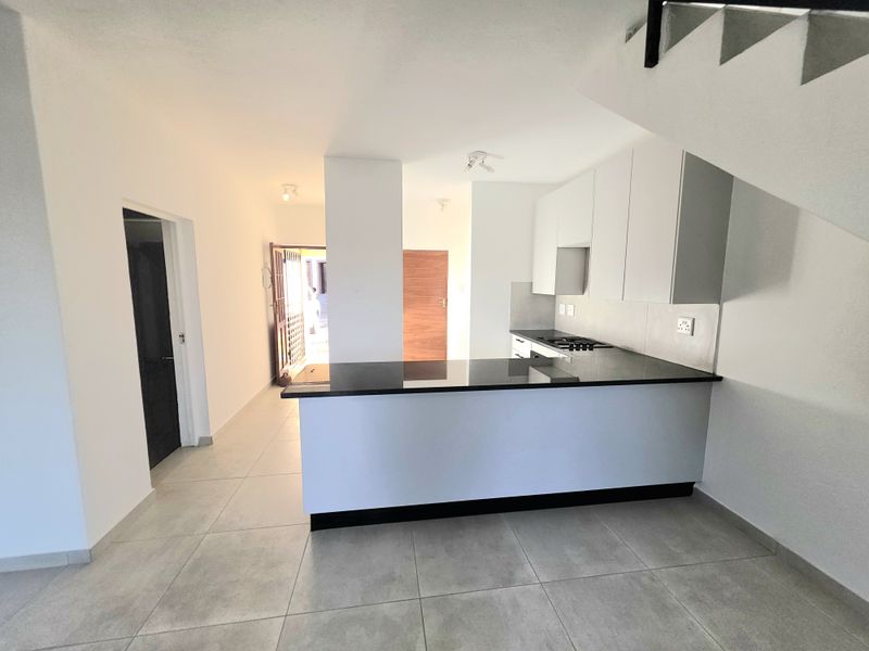 Open-plan kitchen area featuring modern white cabinetry, dark granite countertops, integrated hob, and tiled flooring, situated beneath a staircase.