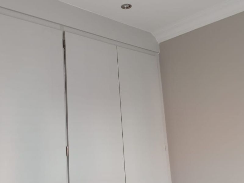 A clean bedroom interior featuring neutral walls, built-in cupboards with modern finishes, and recessed ceiling lighting.
