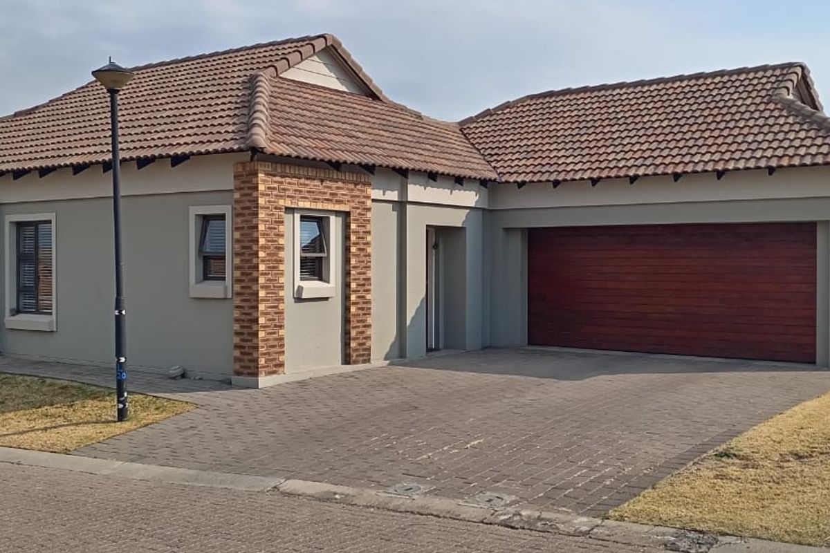 Front elevation of a modern single-story house featuring a tiled roof, brick detailing, paved driveway, and an integrated garage.