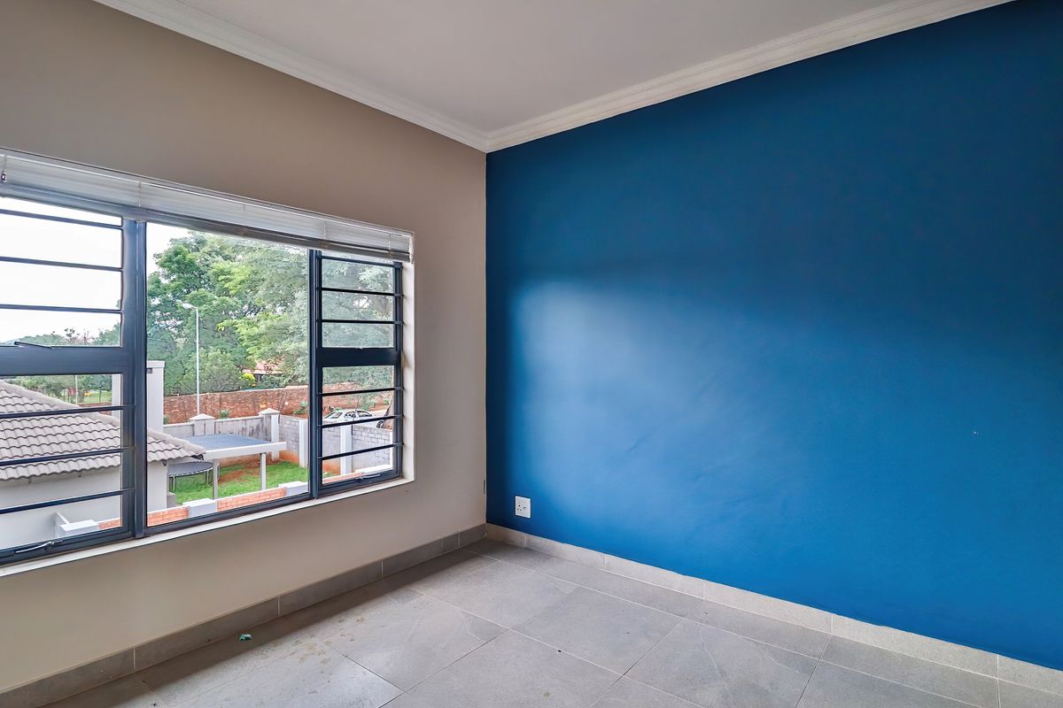 An empty bedroom featuring tiled flooring, a blue accent wall, and aluminium windows with security bars.