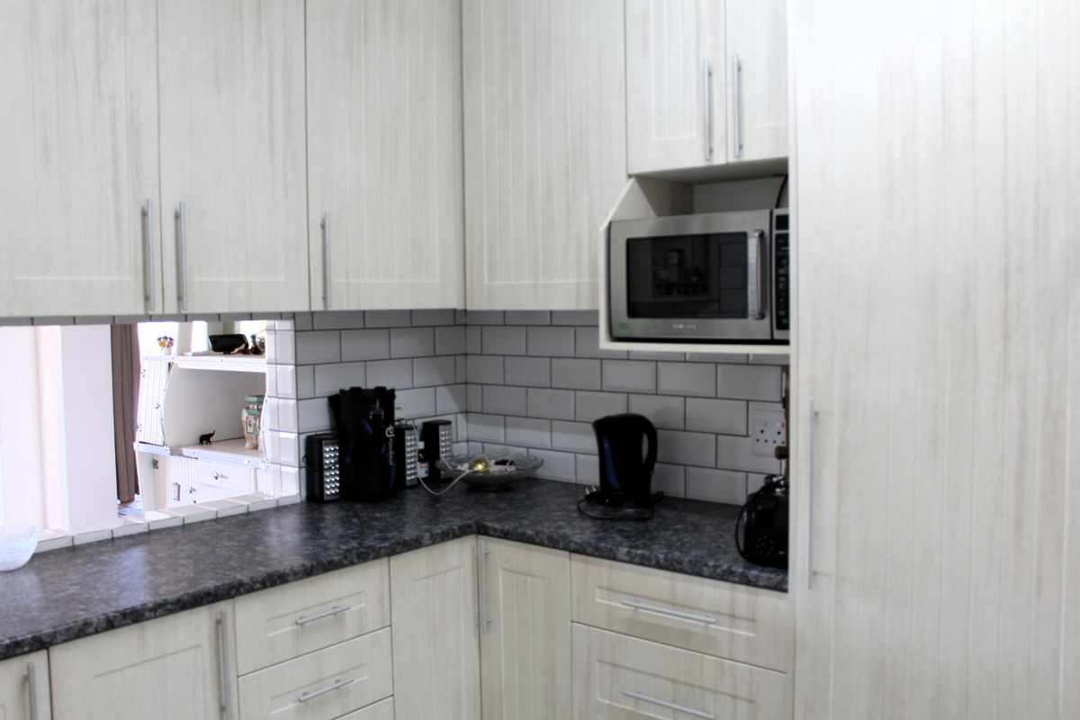 A functional kitchen featuring light-toned cabinetry, dark laminate countertops, and a classic subway tile backsplash with a built-in microwave.