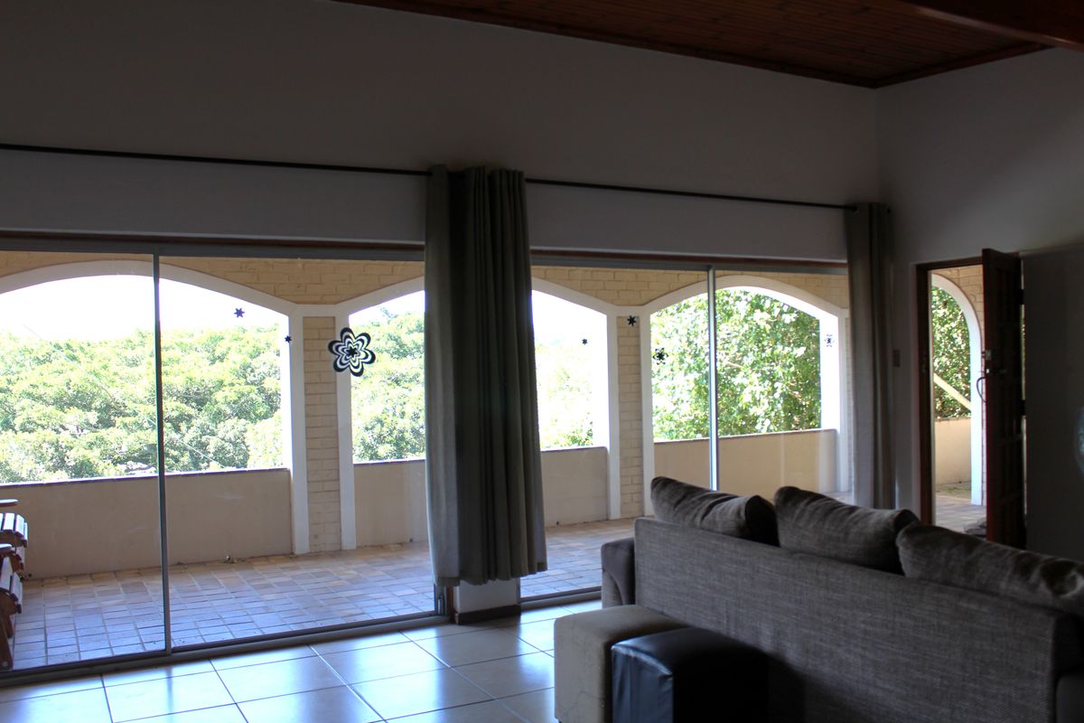 Spacious living area featuring large sliding glass doors that open onto a covered patio with scenic garden views and timber ceiling accents.