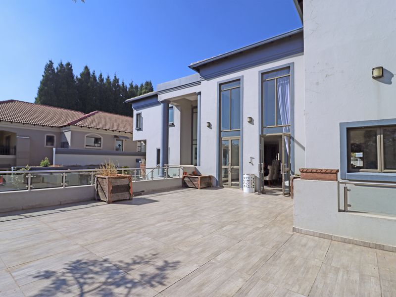 Spacious outdoor patio featuring tiled flooring, glass balustrades with stainless steel railings, and large double-height windows providing access to the interior.