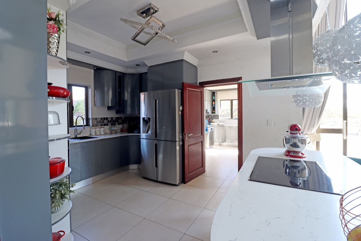 Modern kitchen featuring dark cabinetry, stone countertops, induction cooktop, and integrated extractor fan, with tiled flooring and recessed lighting.