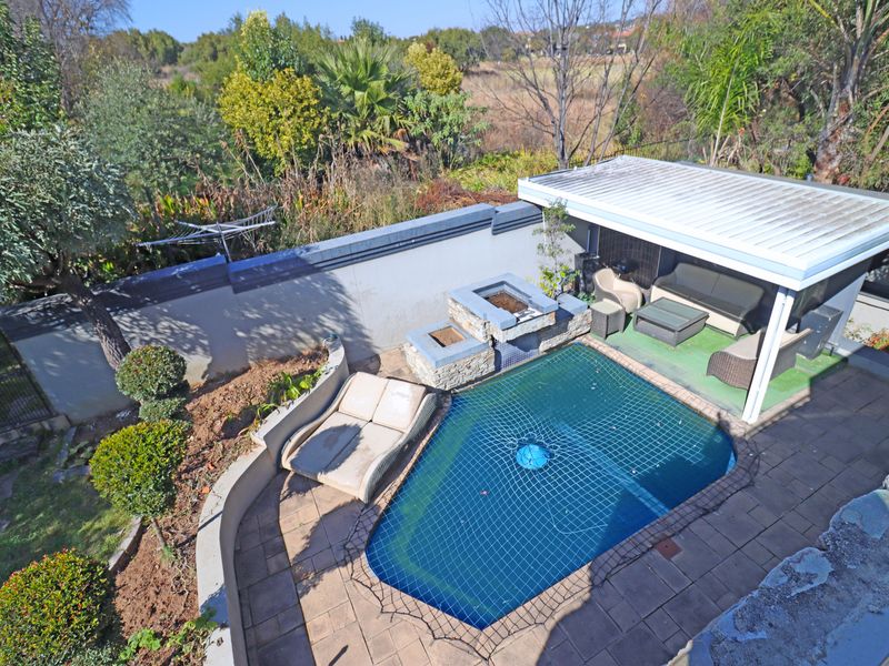 Outdoor entertainment area featuring a swimming pool with safety net, built-in braai, and a covered patio space set within a private garden.