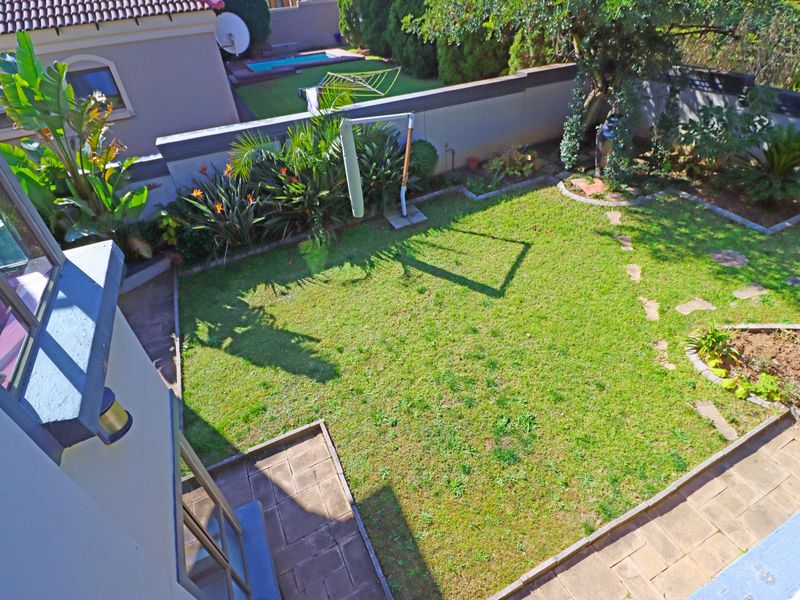 An elevated view of a private rear garden featuring a well-maintained lawn, paved patio area, and perimeter boundary walls.