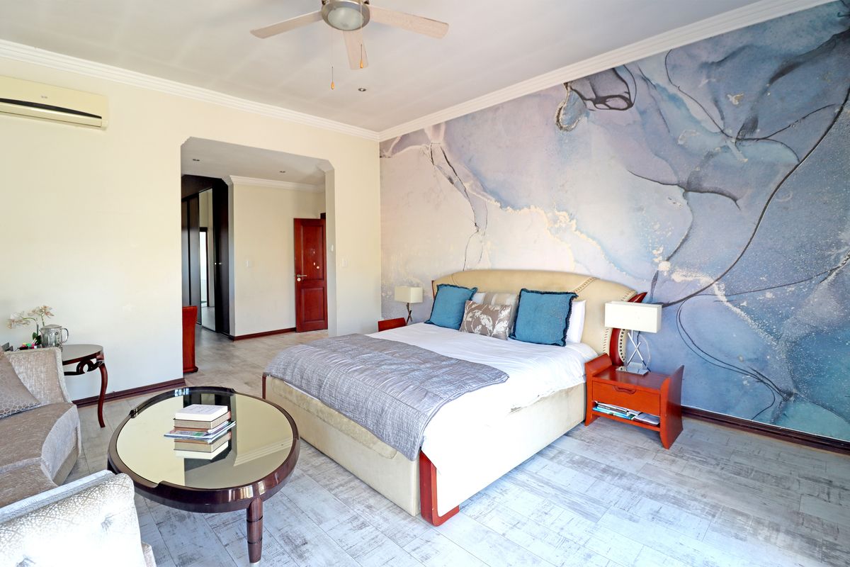 Spacious bedroom featuring a large feature wall, ceiling fan, and wall-mounted air conditioning unit with neutral flooring.