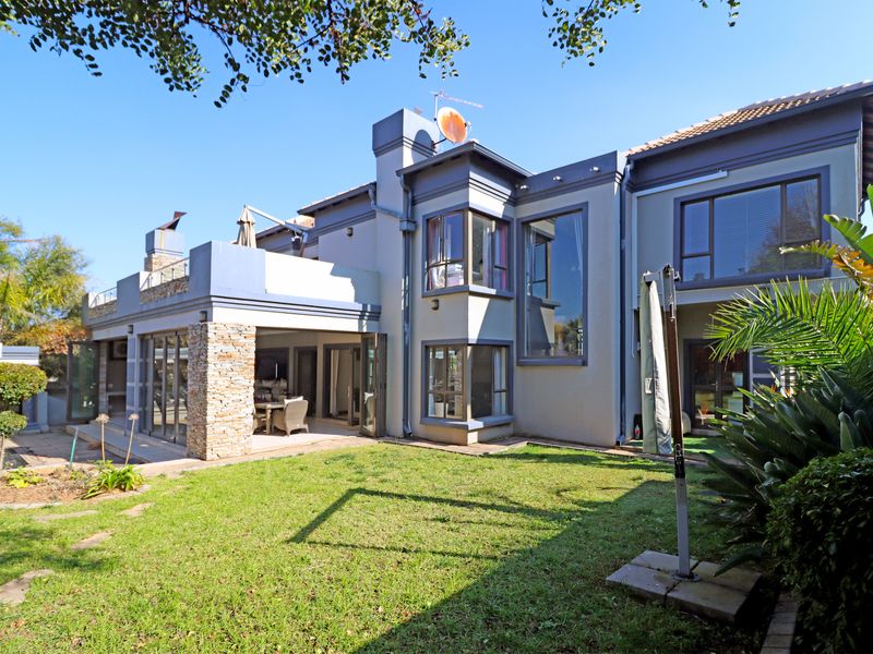 Rear view of a multi-story residential property featuring a covered patio, stone accents, large windows, and a well-maintained garden area.