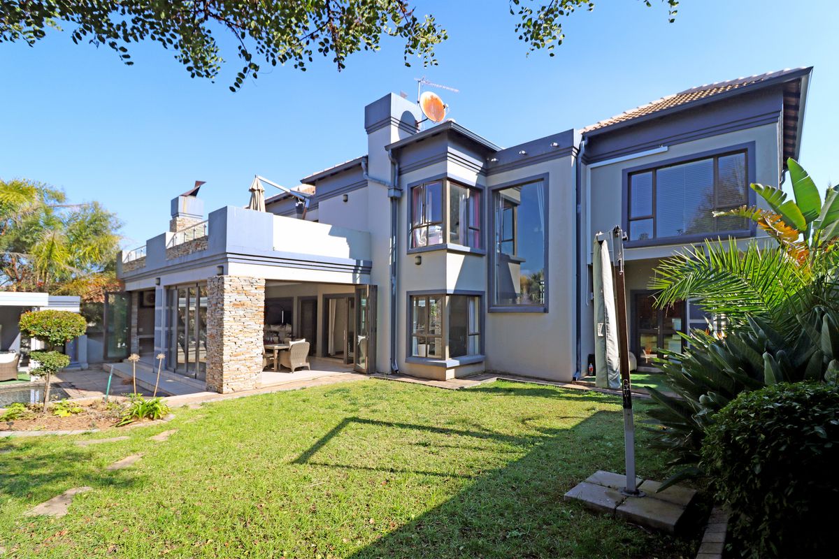 Rear view of a multi-story residential property featuring a covered patio, stone accents, large windows, and a well-maintained garden area.