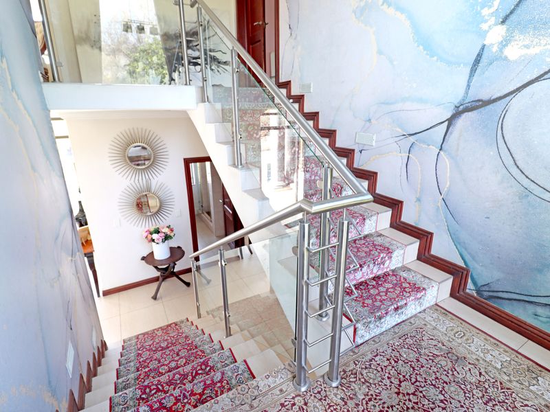A bright entrance hallway featuring a modern staircase with glass balustrades, stainless steel handrails, and decorative feature wallpaper.