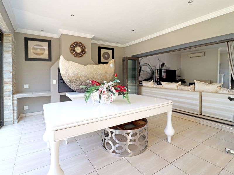 Spacious covered patio featuring tiled flooring, recessed lighting, and a built-in fireplace, seamlessly connecting to the interior living area through large stacking glass doors.