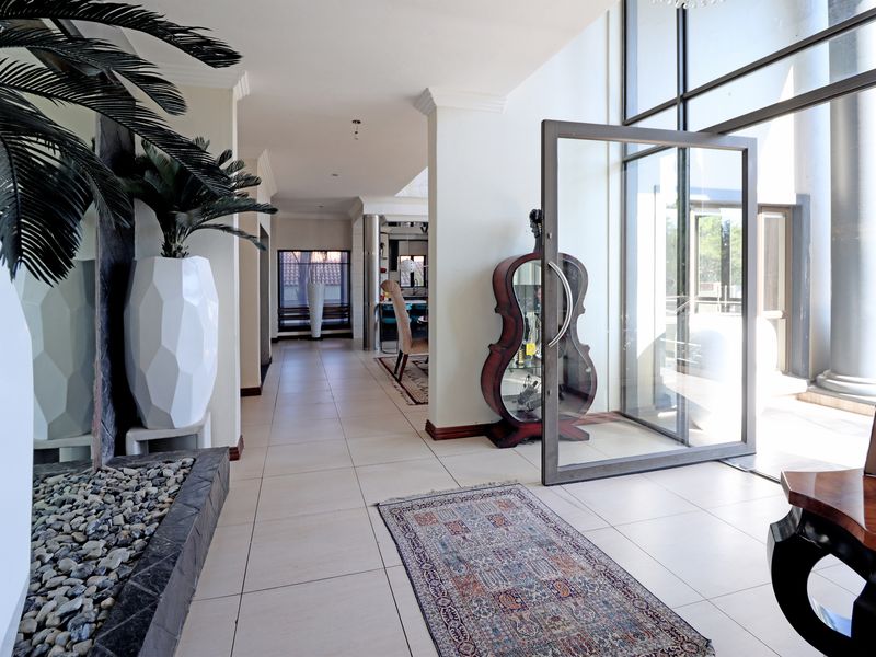 Spacious entrance hall featuring large format floor tiles, a striking pivot door, floor-to-ceiling glass windows, and a built-in internal water feature.