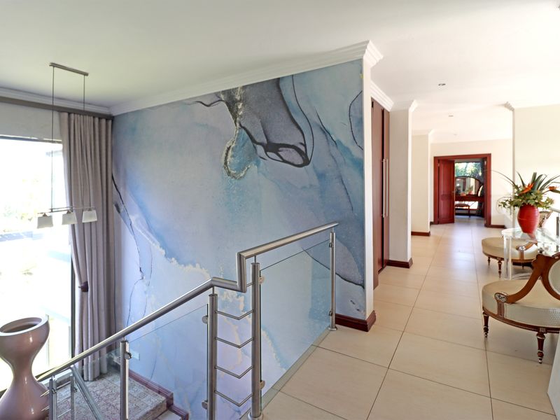 Spacious upper-level hallway featuring a striking abstract feature wall, modern stainless steel and glass balustrade, and neutral tiled flooring.