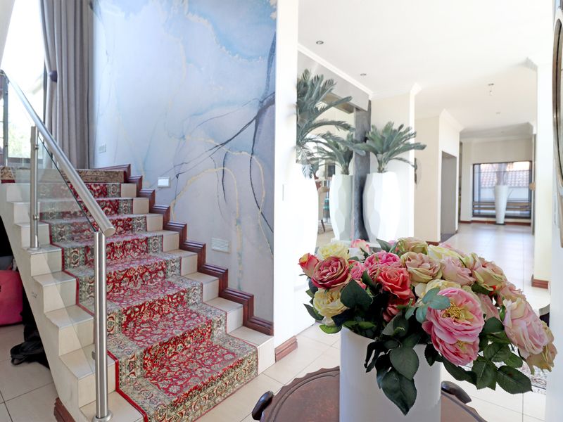 Spacious entrance hall featuring a prominent staircase with a stainless steel balustrade and decorative wall finish, leading into an open-plan living area.