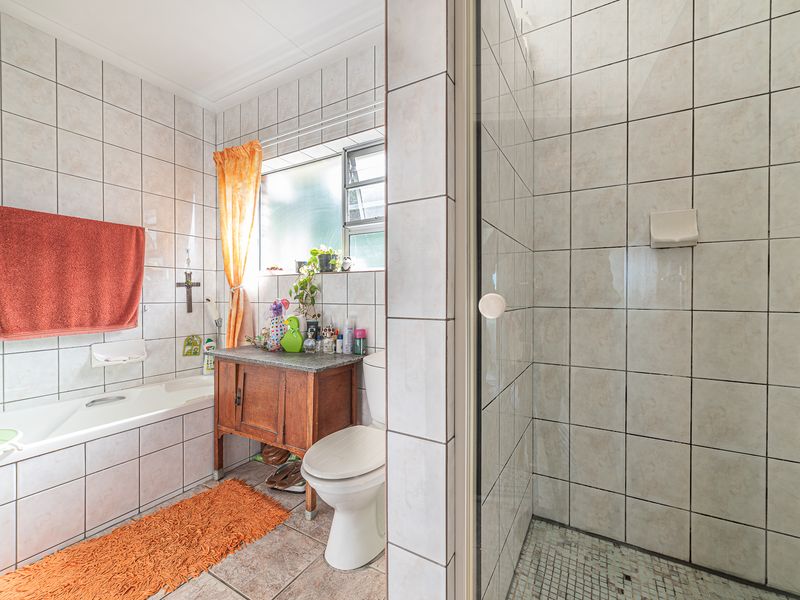 A functional bathroom featuring a bathtub, separate shower enclosure, toilet, and vanity cabinet with tiled finishes throughout.