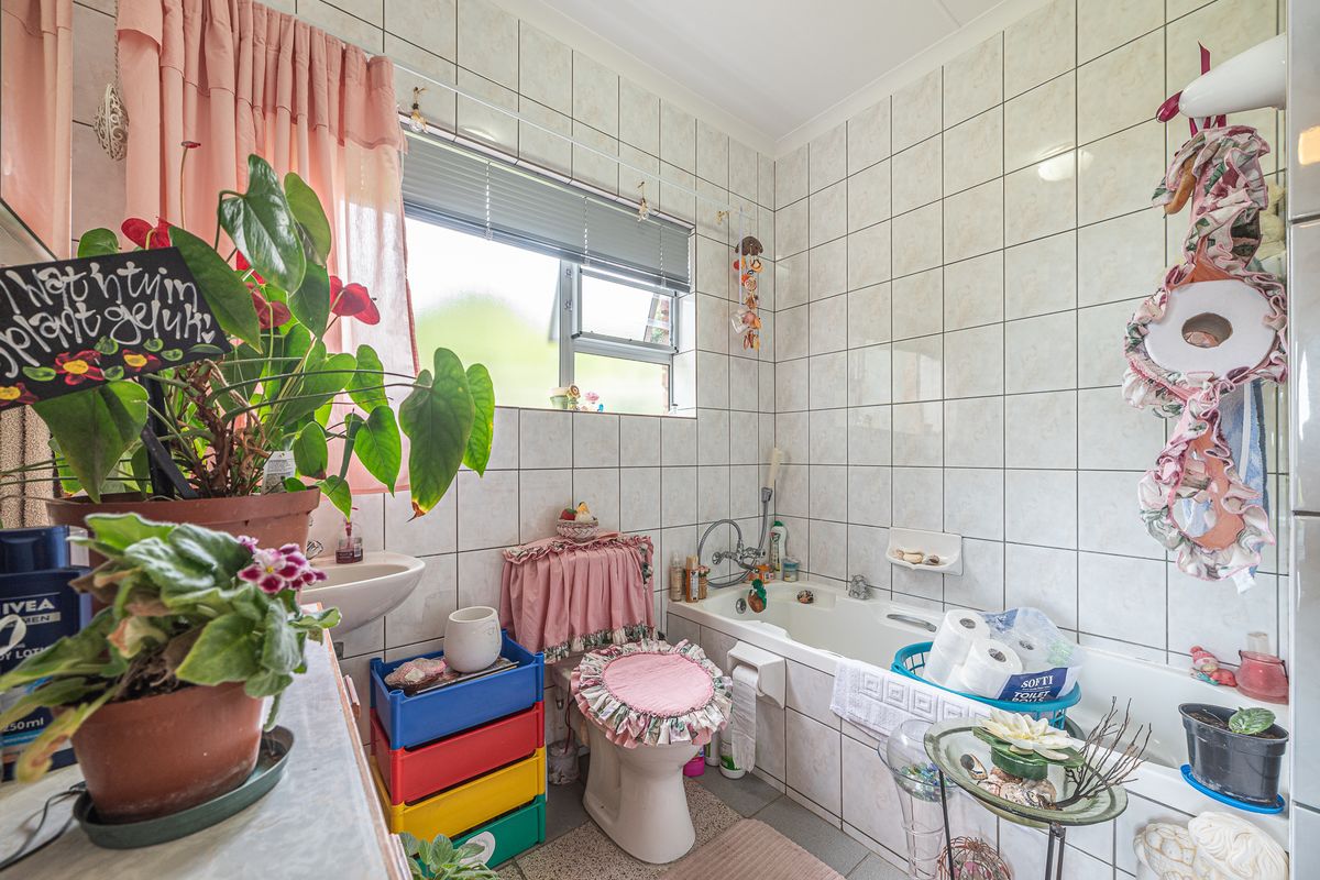 A functional bathroom featuring a bathtub, toilet, and wall-mounted basin with full-height wall tiling and a window for natural light.