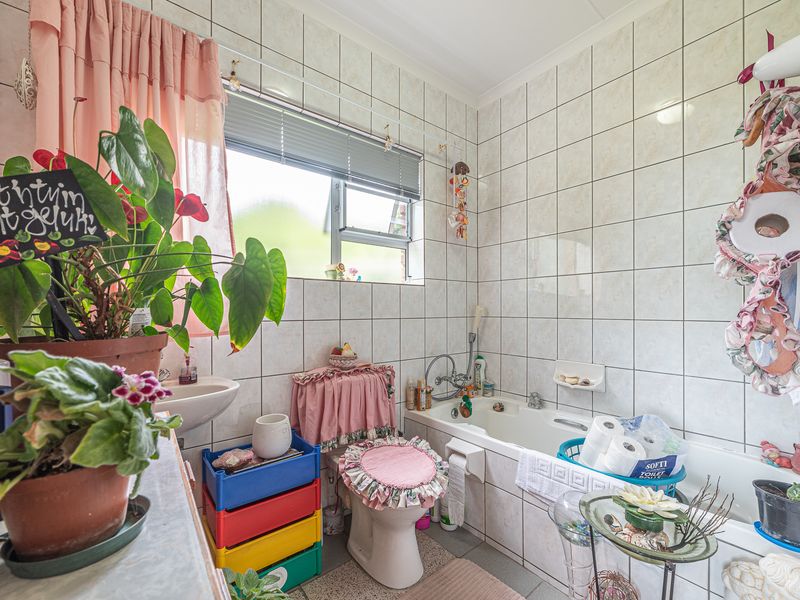 A functional bathroom featuring a bathtub, toilet, and wall-mounted basin with full-height wall tiling and a window for natural light.