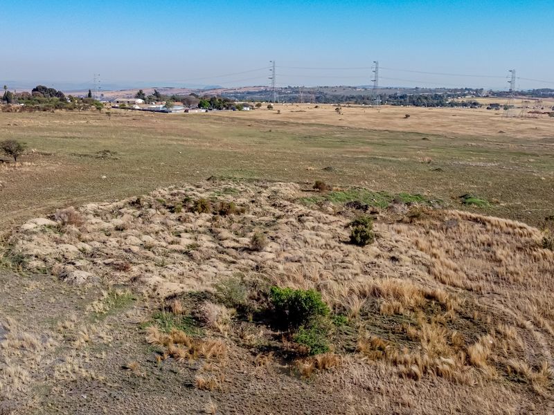 An aerial view of a large, undeveloped residential plot featuring natural grassland and sparse vegetation in a rural setting.