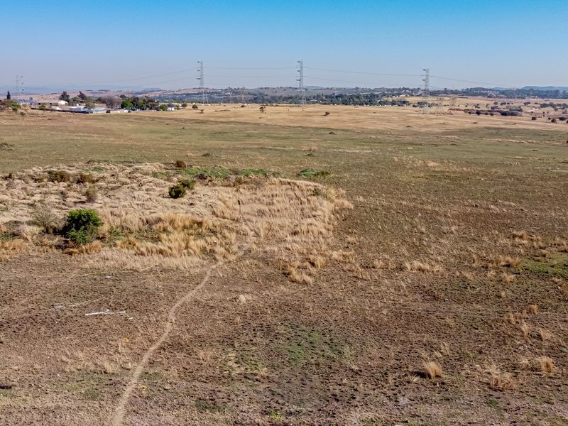 An aerial view of a large, undeveloped residential land parcel featuring open grassland and visible overhead power lines in the distance.