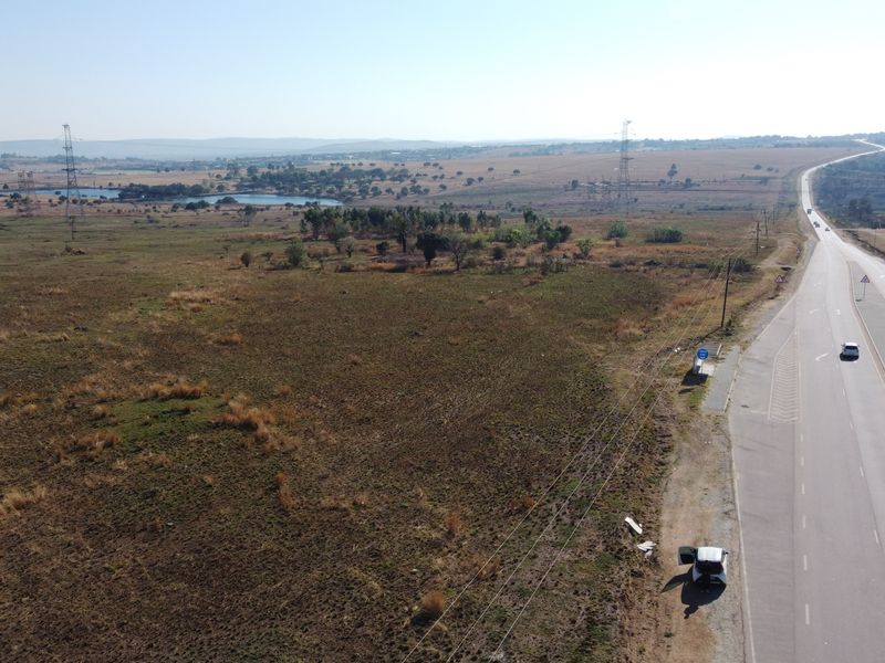 An aerial view of a large, undeveloped residential land parcel adjacent to a main road, featuring open veld and distant landscape views.
