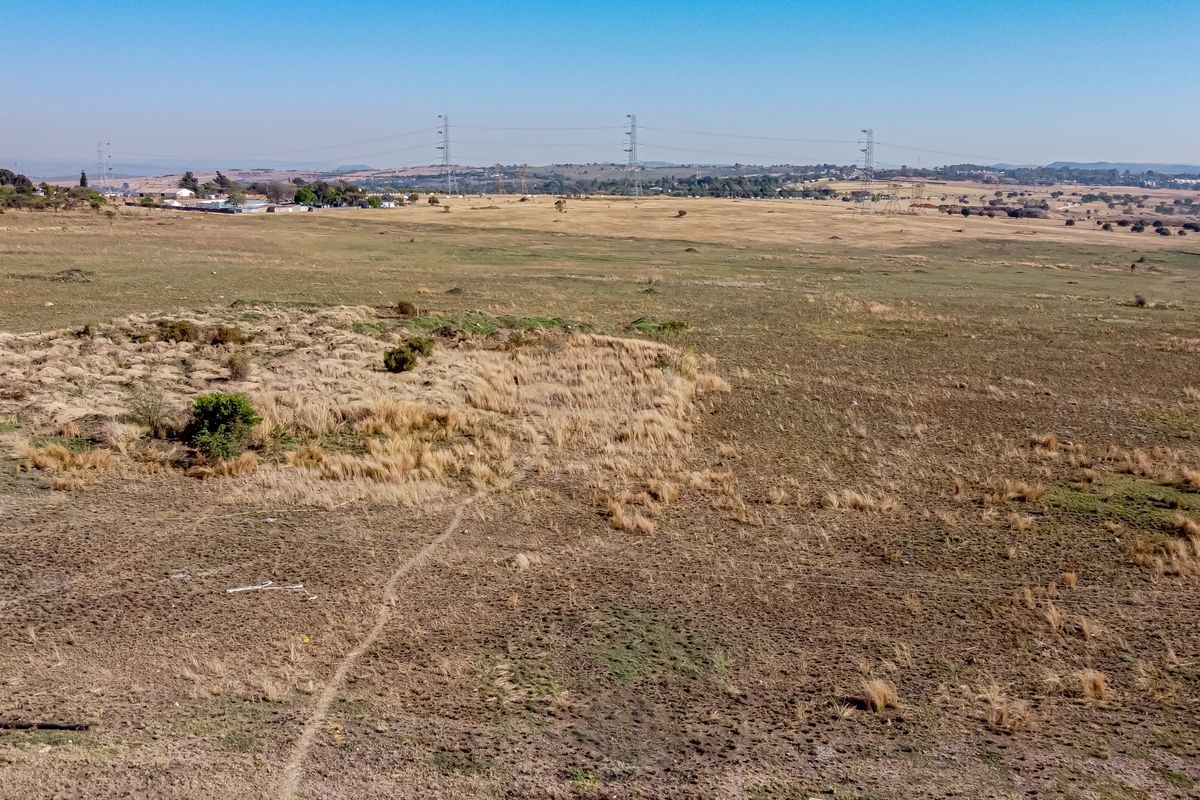 An aerial view of a large, undeveloped residential land parcel featuring open grassland and visible overhead power lines in the distance.