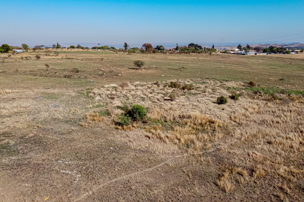 An aerial view of a large, undeveloped residential plot featuring natural dry grass and sparse vegetation, suitable for future development.