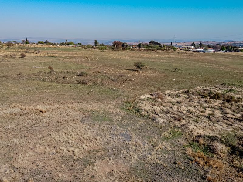 An aerial view of a large, undeveloped residential vacant land plot with natural vegetation and distant landscape views.