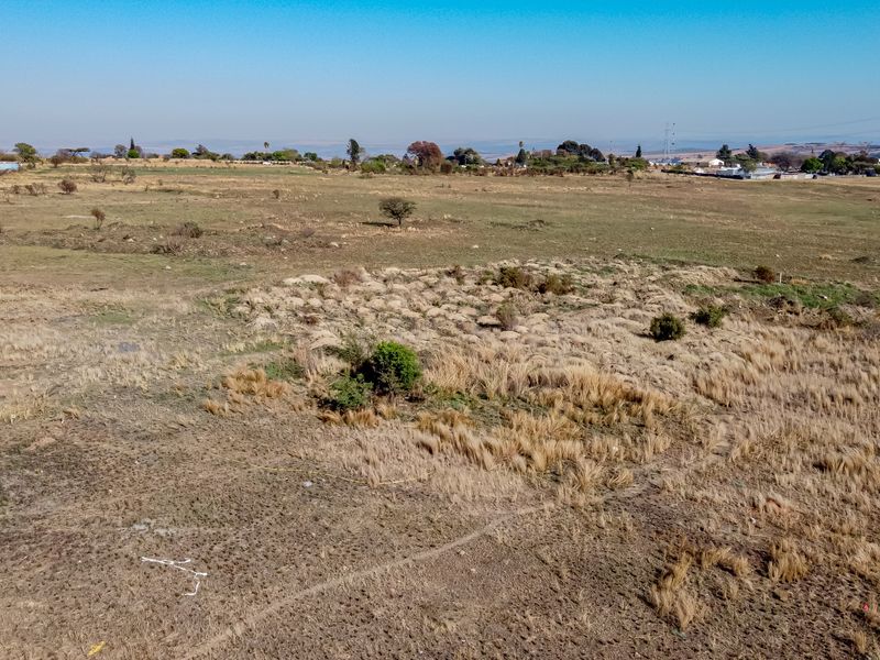 An aerial view of a large, undeveloped residential plot featuring natural dry grass and sparse vegetation, suitable for future development.