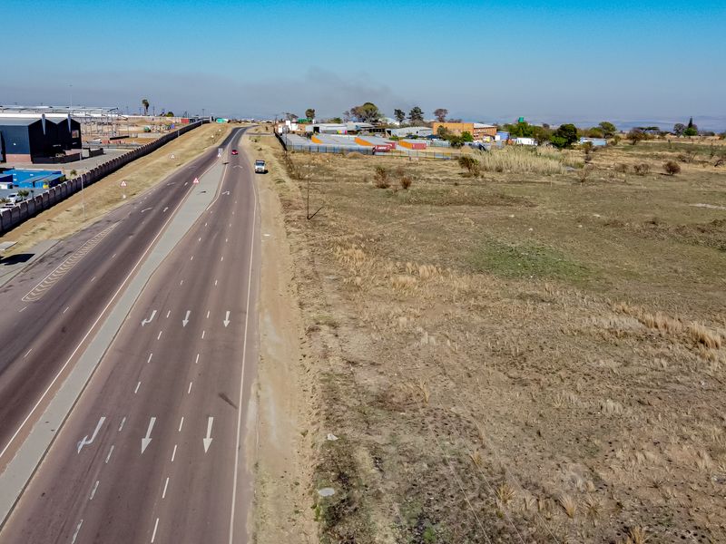Aerial view of a vacant residential land parcel situated adjacent to a major paved road with surrounding industrial and commercial infrastructure.