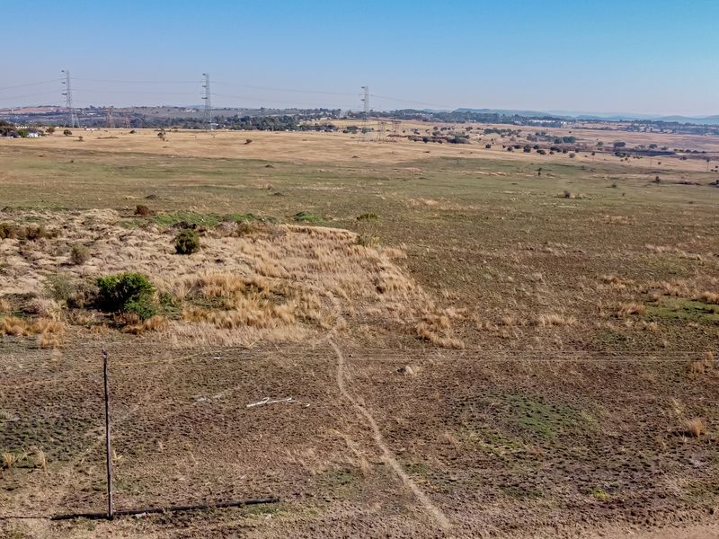 An aerial view of a large, undeveloped residential land plot featuring open grassland and visible utility infrastructure.