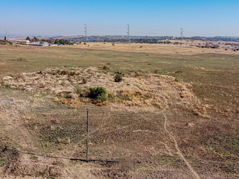 An aerial view of a large, undeveloped residential plot featuring natural grassland and a utility pole.