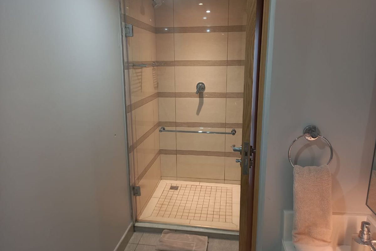 A modern bathroom featuring a walk-in shower with glass enclosure, tiled walls, and a vanity area with a towel ring.