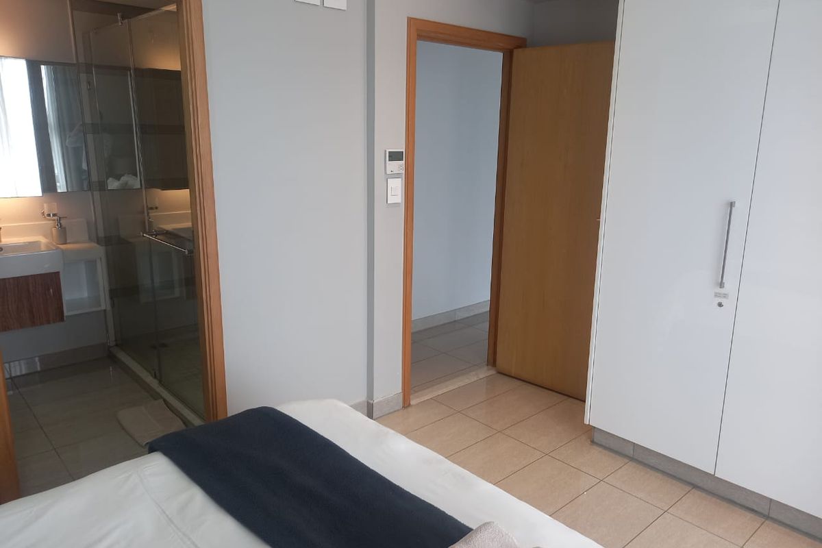 A bedroom featuring built-in white cabinetry, tiled flooring, and an en-suite bathroom with a glass-enclosed shower.