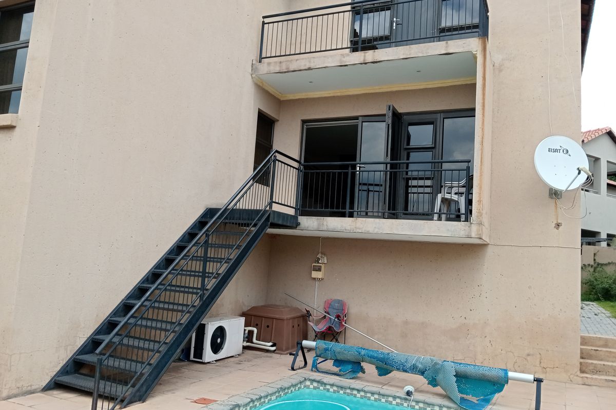 Rear exterior view of the house featuring a swimming pool, a metal staircase leading to a balcony, and sliding door access to the upper level.