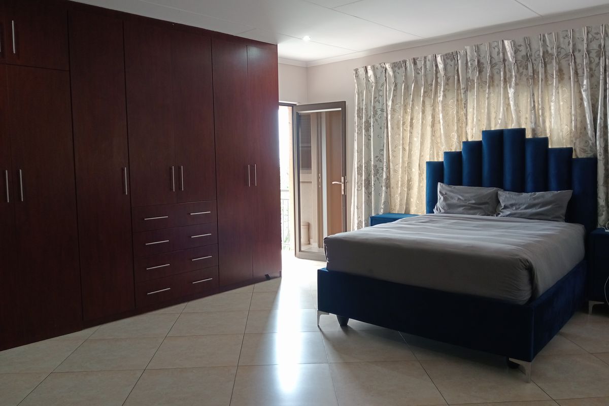 Spacious bedroom featuring extensive dark wood built-in cupboards, tiled flooring, and direct access to an outdoor balcony area.
