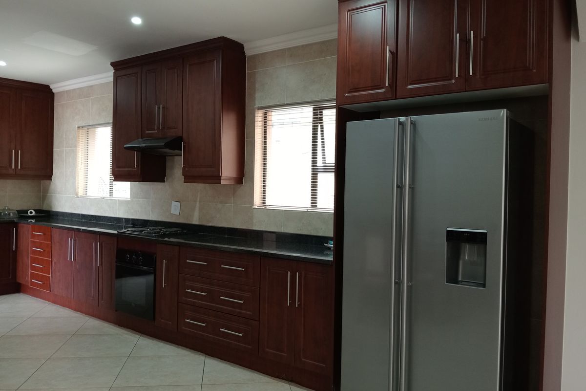 A well-maintained kitchen featuring dark wood cabinetry, granite countertops, built-in oven, hob, and extractor fan with neutral tiled flooring and backsplash.