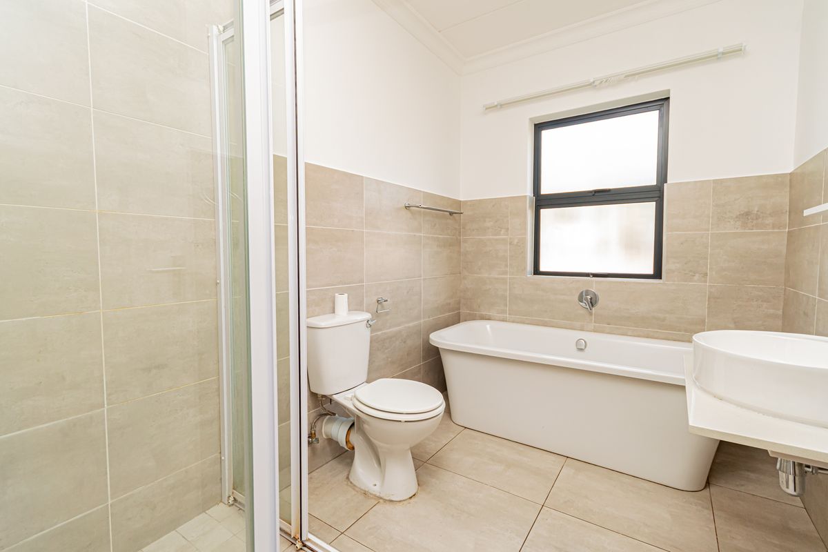 A clean, modern bathroom featuring a separate shower enclosure, a freestanding bathtub, and a wall-mounted basin with neutral floor-to-ceiling tiling.