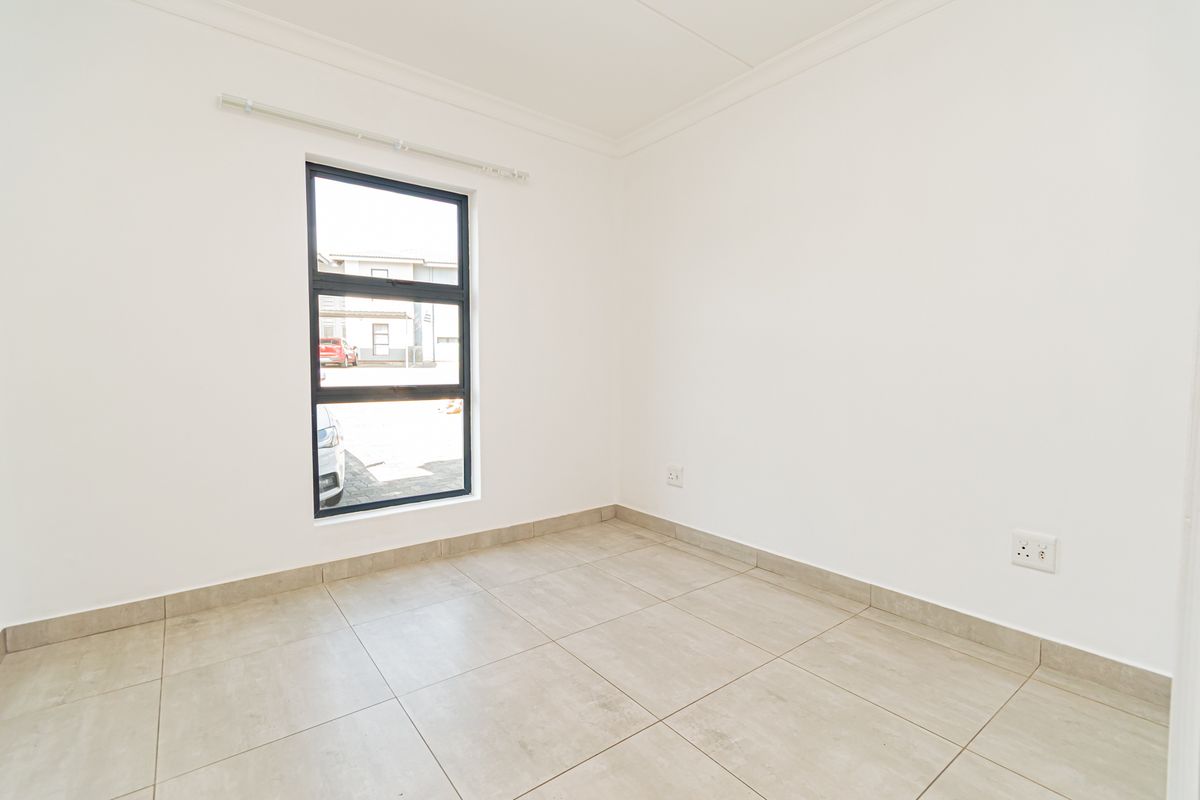 A bright, empty bedroom featuring neutral tiled flooring, clean white walls, and a modern aluminium-framed window.