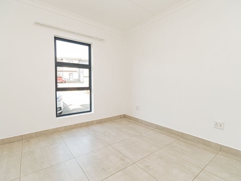 A bright, empty bedroom featuring neutral tiled flooring, clean white walls, and a modern aluminium-framed window.