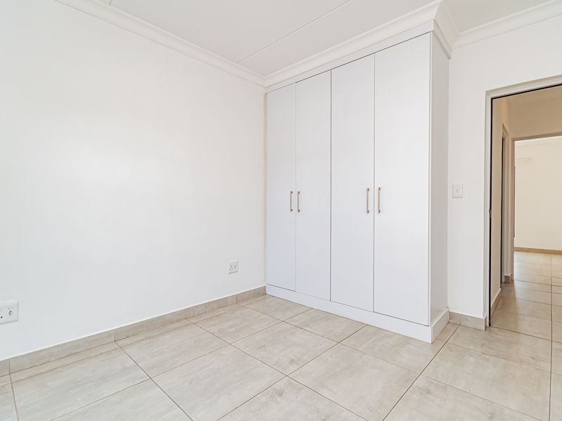 A clean, bright bedroom featuring neutral tiled flooring, crisp white walls, and a modern built-in wardrobe with sleek hardware.