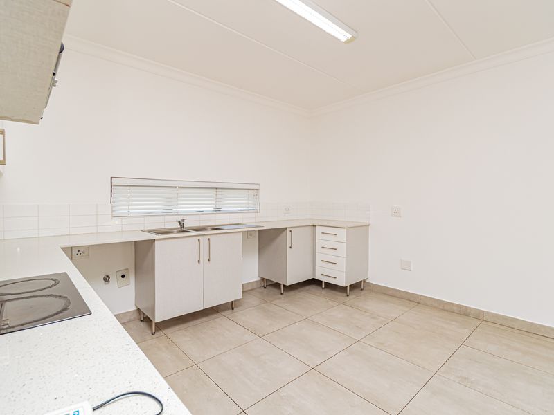 A clean, functional kitchen featuring neutral cabinetry, laminate countertops, an integrated electric hob, and tiled flooring, offering a bright and well-maintained workspace.