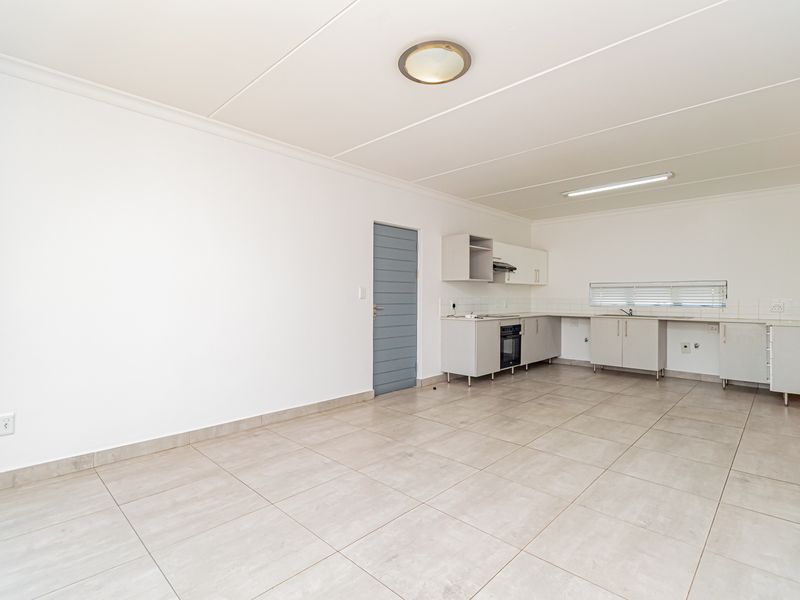 An open-plan kitchen and living area featuring neutral tiled flooring, built-in cabinetry, and a functional kitchen layout with an integrated oven and extractor fan.