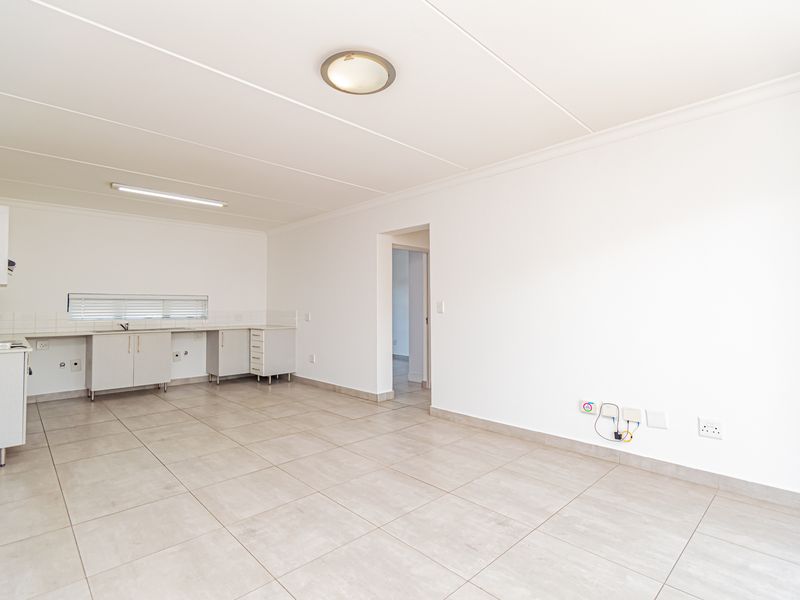 An open-plan living and kitchen area featuring neutral tiled flooring, built-in cabinetry, and clean white walls, offering a versatile blank canvas for interior design.