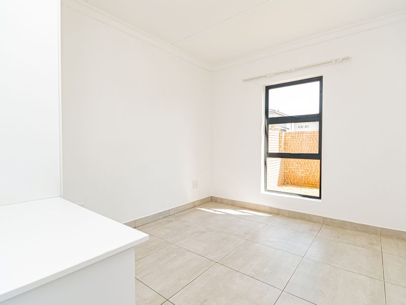 A bright, empty bedroom featuring neutral tiled flooring, clean white walls, and a built-in cabinet, offering a versatile space ready for personalization.