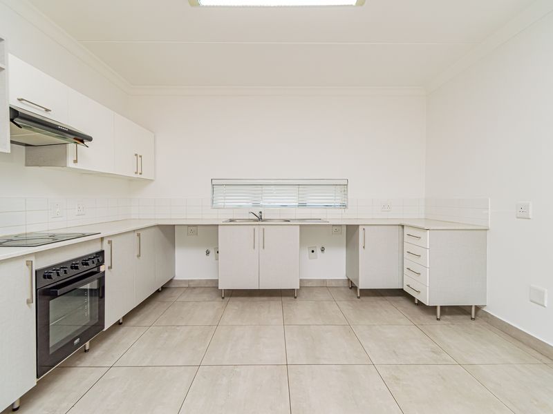 A clean, modern kitchen featuring white cabinetry, built-in oven and hob, tiled flooring, and ample counter space, presented in an empty, move-in ready condition.