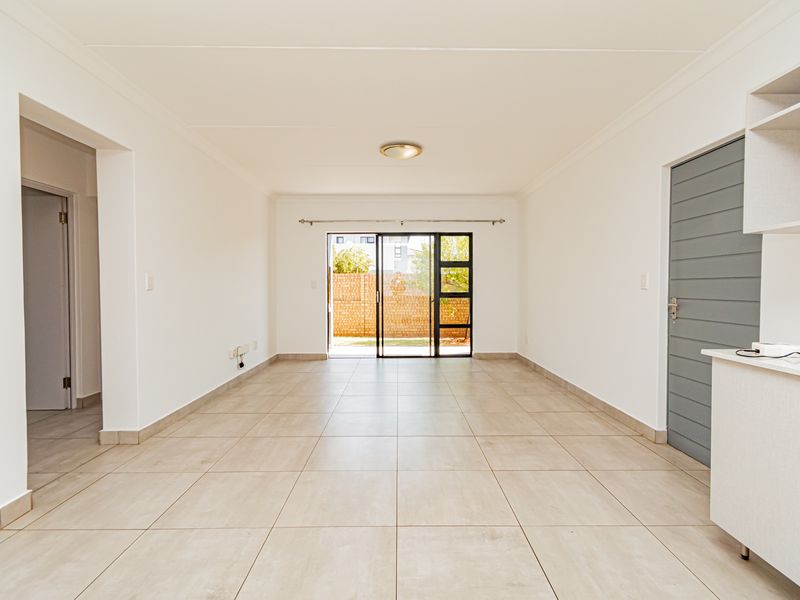 A bright, open-plan living area featuring neutral tiled flooring, clean white walls, and a sliding glass door providing access to the rear exterior.